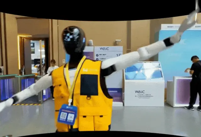 A humanoid guide robot in a yellow vest works inside a WAIC venue.